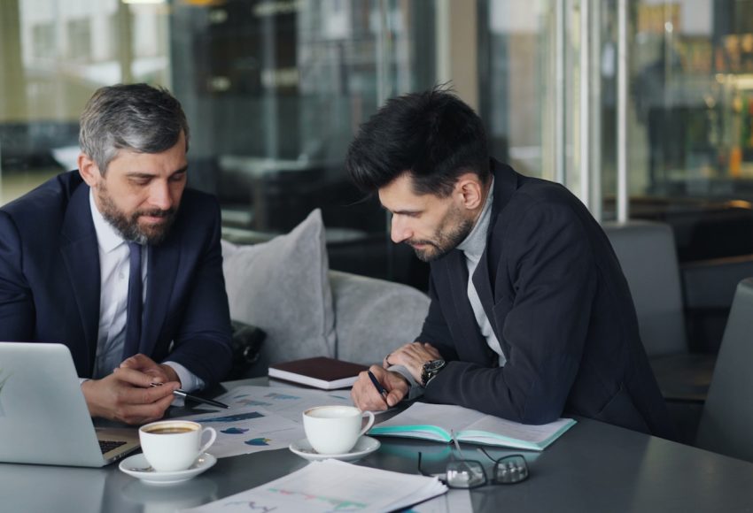 two men sitting at a table working on a laptop